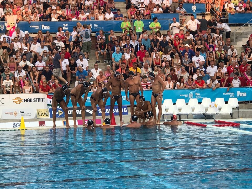 Darkside water polo team discussing game adjustment strategy during a break at the 2017 FINA World Championships in Budapest, with spectators in the stands.